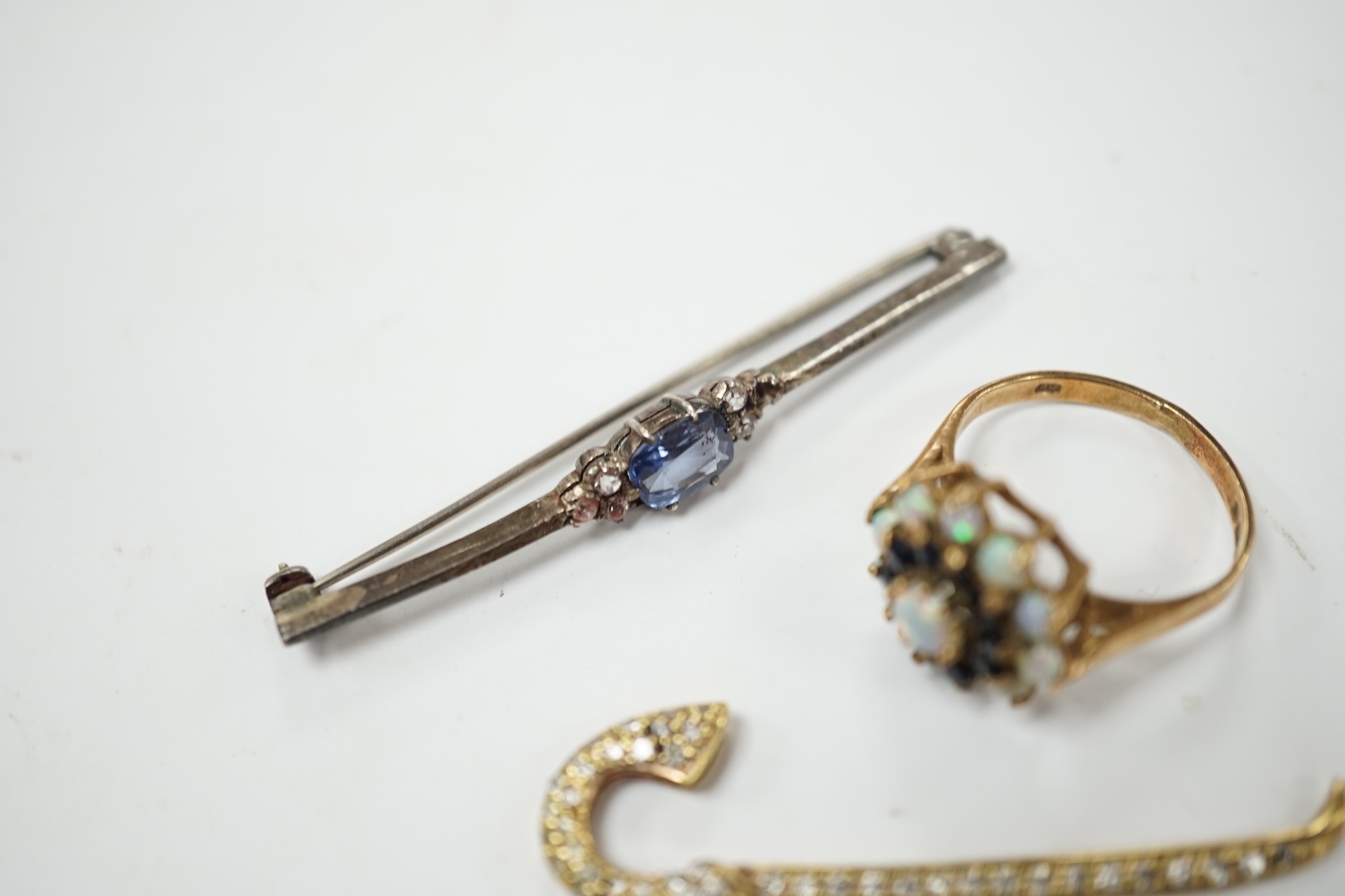 A yellow metal and pave set diamond miniature walking cane, 43mm, together with a 9ct gold, white opal and sapphire cluster set ring and a two colour sapphire set white metal bar brooch. Condition - poor to fair
